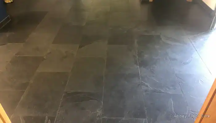 Significant buildup of discoloured floor wax along slate tile edges and grout
